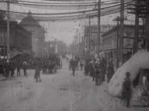 Crowded street lined with buildings and overhead power lines post-disaster.