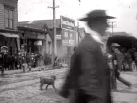 Pedestrians and a dog walking on a cobblestone San Francisco street in 1906.