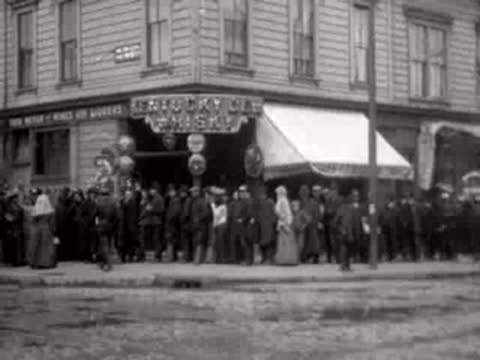 Crowd of people gathered outside a building with a storefront in San Francisco, 1906.