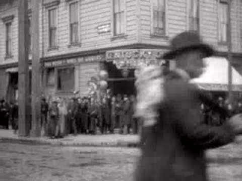 Man walking past a crowd gathered in front of a San Francisco building in 1906.
