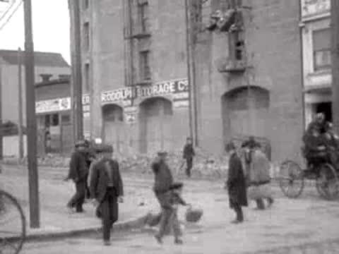 Pedestrians walking past a damaged brick building in San Francisco, 1906.