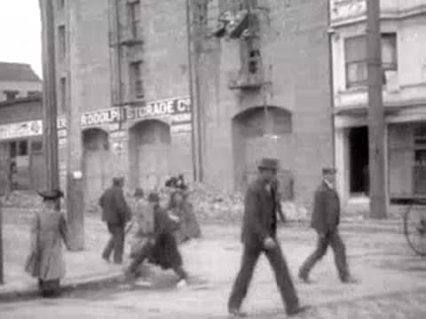 People walking on a street near a damaged brick building in San Francisco, 1906.