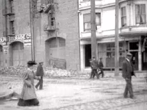 People walking on a street past a building in San Francisco, 1906.