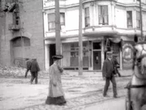Pedestrians walking past a building and horse-drawn carriage in San Francisco, 1906.