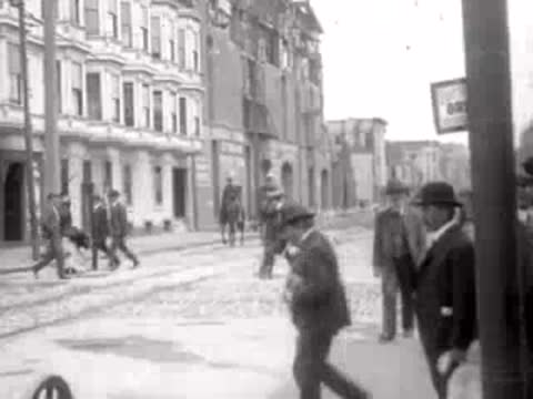 pedestrians on cobblestone street past buildings, historical footage