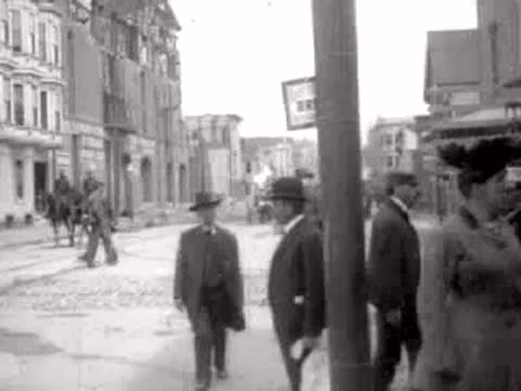 people walking along city street past buildings, historical footage