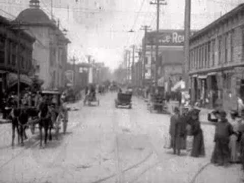 Pedestrians and horse-drawn carriages on a bustling urban street.