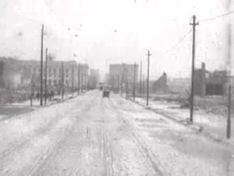 pedestrian walking on wide street with ruined buildings, historical footage
