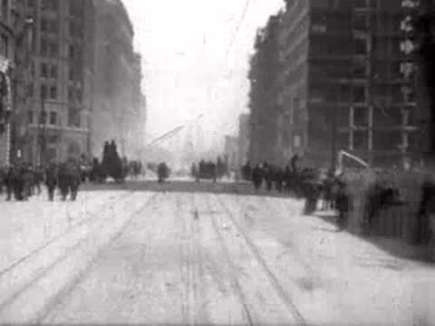 street between tall buildings with crowds of people, historical footage