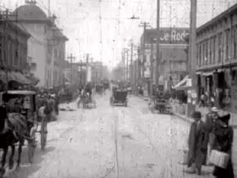 People walking and carriages driving down a busy city street.