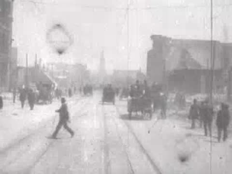 Street view after San Francisco earthquake, pedestrians walking among debris, horse carriages.