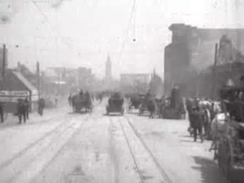 Street view after San Francisco earthquake, horse carriages, debris, pedestrians.