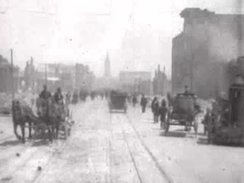 Street view after San Francisco earthquake, horse-drawn vehicles, pedestrians, rubble.