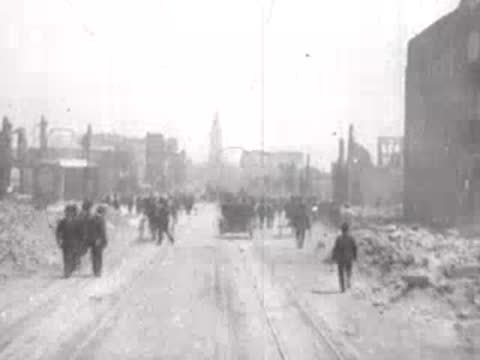 Street view after San Francisco earthquake, pedestrians walking among rubble, horse carriages.