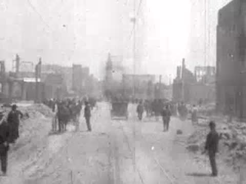 Street view after San Francisco earthquake, horse carriages, rubble piles, pedestrians.