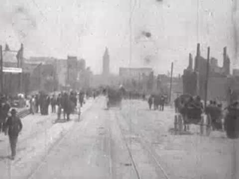 Street view after San Francisco earthquake, horse carriages, debris, pedestrians.