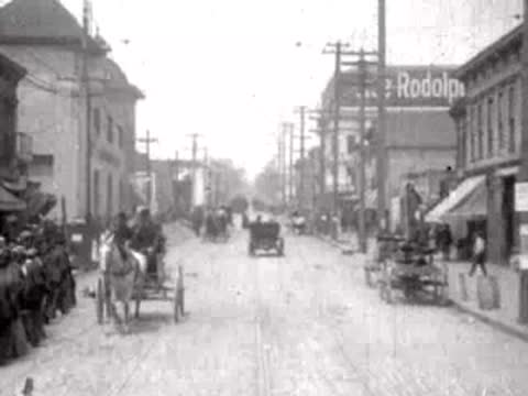 Horse carriages and pedestrians on a street with damaged or dusty conditions.