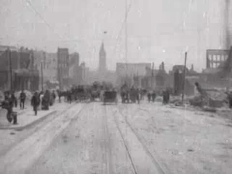 Street view after San Francisco earthquake, horse carriages, debris, pedestrians.