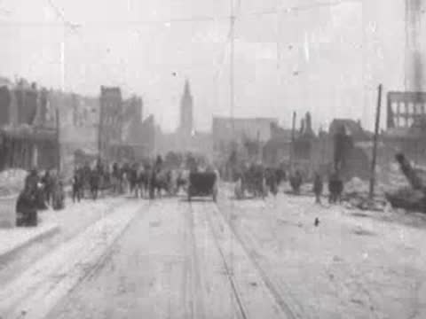 Street view after San Francisco earthquake, horse carriages, pedestrians, rubble piles.