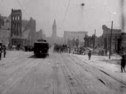Tram moving forward on Market Street surrounded by earthquake-damaged buildings and pedestrians.