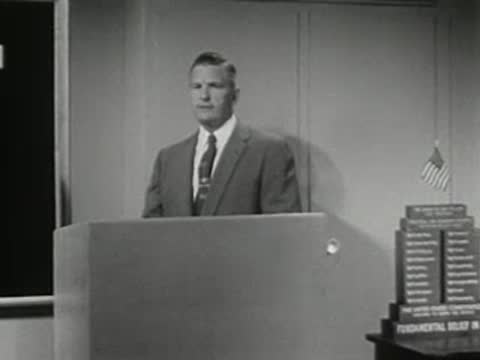 Man standing behind podium in a studio with display on the right