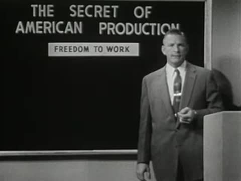 Man standing in front of blackboard with text about American production