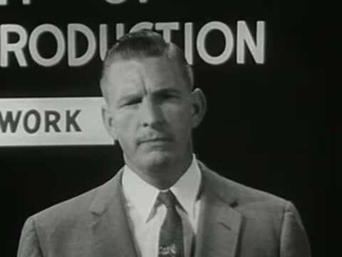 Man speaking in close-up in front of a blackboard with text
