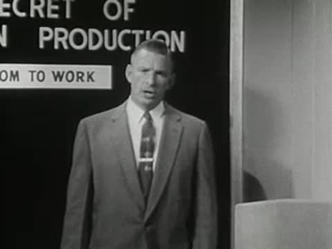 Man speaking in front of blackboard with text 'SECRET OF PRODUCTION'