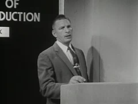Man standing behind podium in front of a blackboard with text