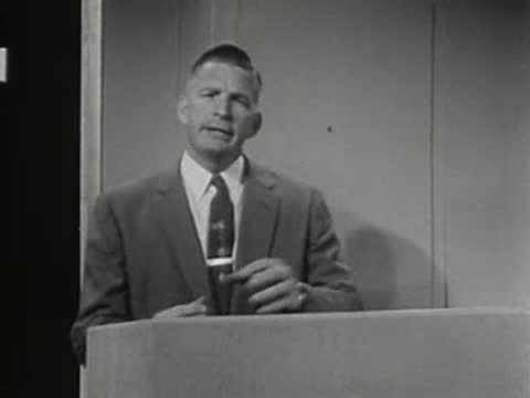 Man standing behind podium speaking in a studio setting