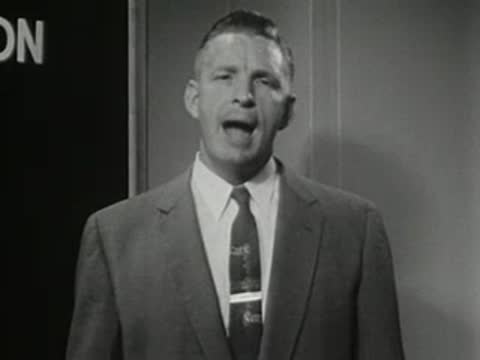 Man speaking behind podium with blackboard and text in background