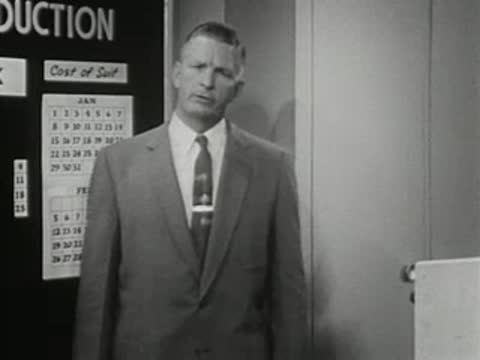 Man in suit standing before a calendar chart, 1950s