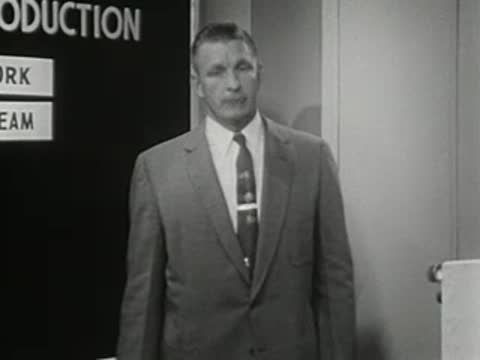 Man standing and speaking near a chart board, 1950s film