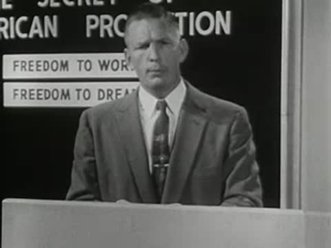 Man standing at a podium with production chart, 1950s film