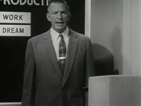 Man standing at a podium in front of a chart, 1950s