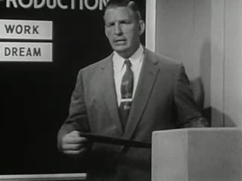 Man holding a strip label in front of a chart, 1950s