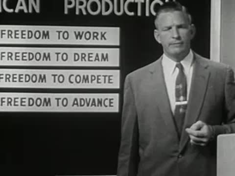 medium close-up of a man in suit speaking in front of text board