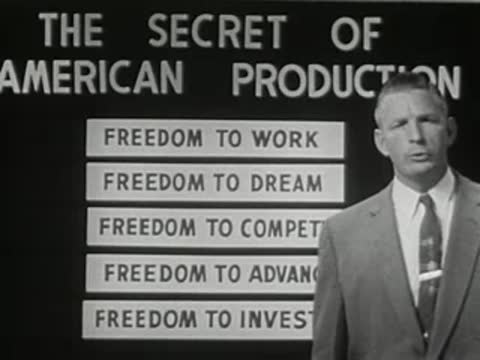 man in suit speaking next to a board listing american production keys