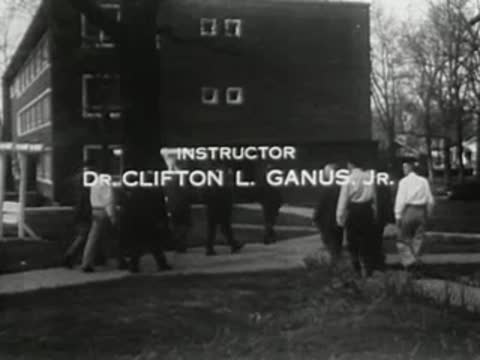 Text credits appear over a shot of people walking toward a multi-story building.