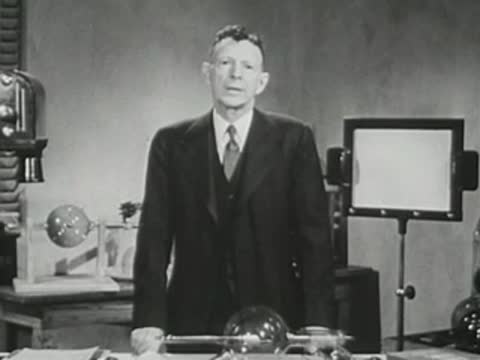 Presenter in a suit standing in front of a screen and laboratory table.