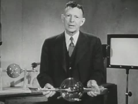 Presenter holding a large spherical glass vacuum tube in front of screen.