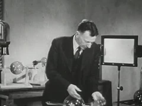 Presenter putting down the large spherical tube and picking up another device.