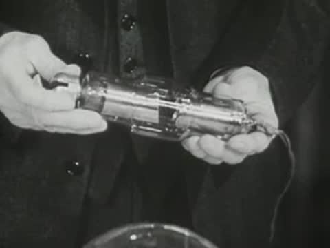 Close-up of hands manipulating a smaller specialized metal and glass electronic tube.