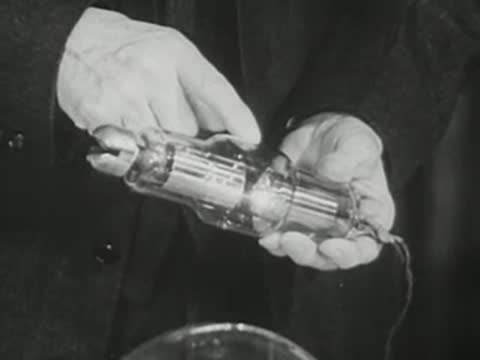 Close-up of hands pointing to specific parts of a small glass electronic tube.