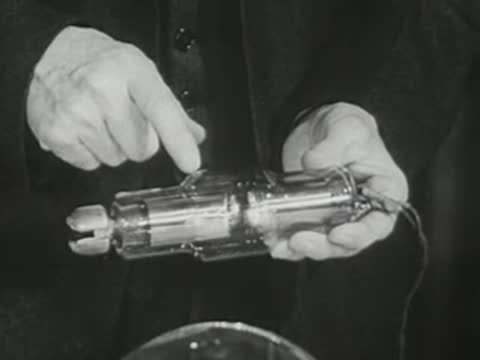 Lecturer in suit points to features of an X-ray tube in hand.