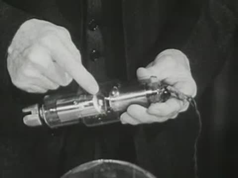 Lecturer in suit points to the central section of an X-ray tube in hands.