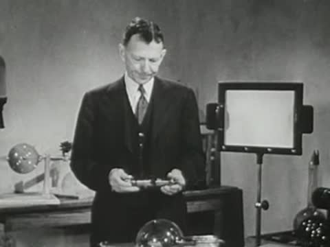 Lecturer holds a spherical glass object and an X-ray tube in his hands.