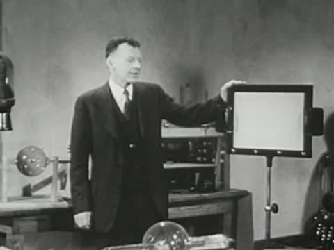 Lecturer stands beside an illuminated display screen in a laboratory setting.