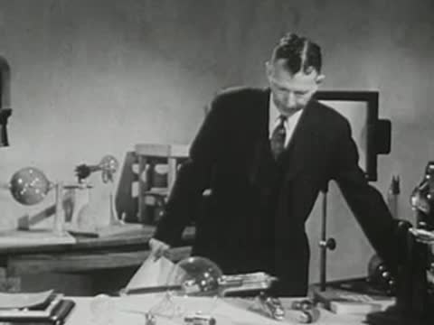 Lecturer places paper down and gestures while standing at the laboratory bench.