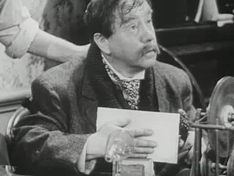 Man with mustache examining a glass plate in historical setting.